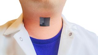 photo shows a shiny black patch made up of small squares stuck to a man's throat; he's wearing a white button down over a blue t shirt