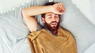 The image shows a man sleeping on his back with his mouth open and his arm above his head