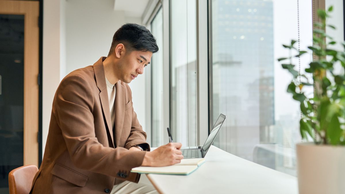 A young man working on laptop in office writing notes