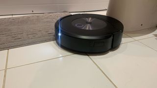 En svart iRobot Roomba Combo j7+ håller på att göra rent ett vitt klinkergolv.