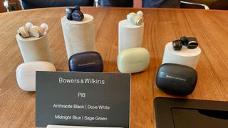 Bowers & Wilkins Pi8 earbuds, held in a hand on grassy background