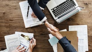 Two people shaking hands across a corporate desk