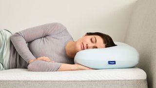 The image shows a woman resting her head on the Casper Hybrid Pillow with Snow Technology