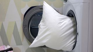 Image shows a white pillow being placed inside a washing machine for washing