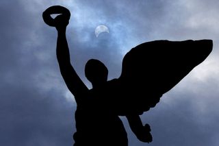 The moon makes its way in front of the sun during a total solar eclipse framed above the angel atop the Princes' Gates, in Toronto