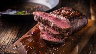 A medium rare rib eye steak, sliced to show th pink center on a wooden board