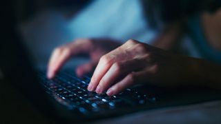 Man typing in password on keyboard in low light.