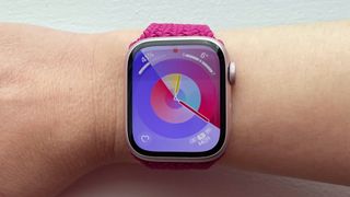 A magenta-colored Apple Braided Solo Loop is attached to a light pink Apple Watch , facing forward on the wearer's wrist.