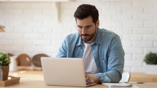 Man wearing glasses, sitting at a table and using a laptop