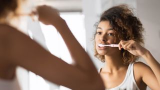 A woman brushing her teeth in a mirror as part of her nighttime routine