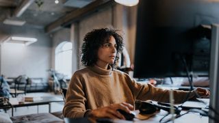 Female python software developer working at computer in open plan office space.