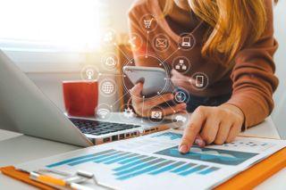 Woman holds mobile phone while pointing to a printed graph