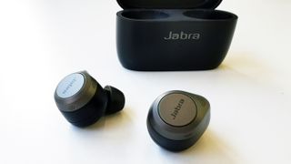 Ett par jabra elite 85t ligger bredvid sitt tillhörande laddningsfodral.