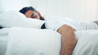 A man takes a nap on a white bed during the day