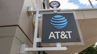 A black AT&amp;T sign with its logo in bright blue hanging outside a brick store 