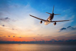 Airliner flying over water with sunset