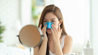 young women applying a grease-removing cloth to her nose while looking in a small mirror