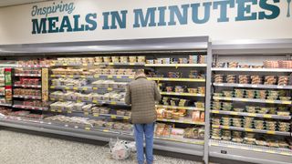 A man stands in a processed food aisle with a sign above reading "Inspiring Meals in Minutes"