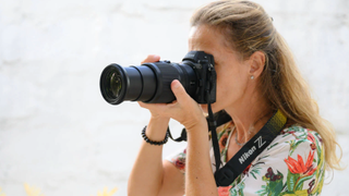 The Nikon Z 24-200mm f/4-6.3 lens attached to a Nikon camera held up to person&#039;s eye with summer ocean backdrop