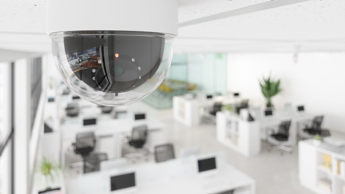 Workplace surveillance and monitoring concept image showing a CCTV camera with an open place office space in the background.