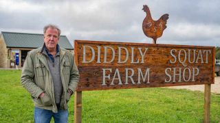 Jeremy Clarkson standing next to the Diddly Squat Farm Shop sign.