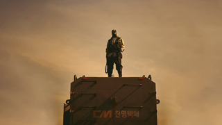 Masked figure stands on truck in desert