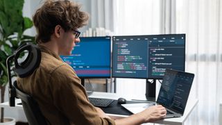 software developer working at laptop with external monitors to his side