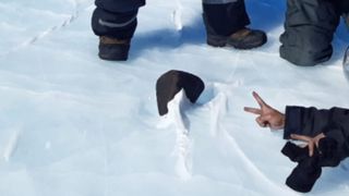 A close-up of the black-colored 16.7-pound meteorite resting on the snow.