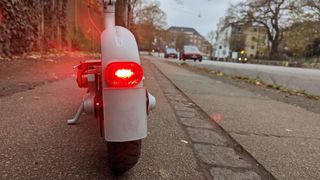 Mi Electric Scooter 3 står på et fortov med baglygten tændt tæt på kameraet