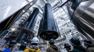 closeup of a large black conical spacecraft inside a hangar, with seven people in hardhats in the foreground