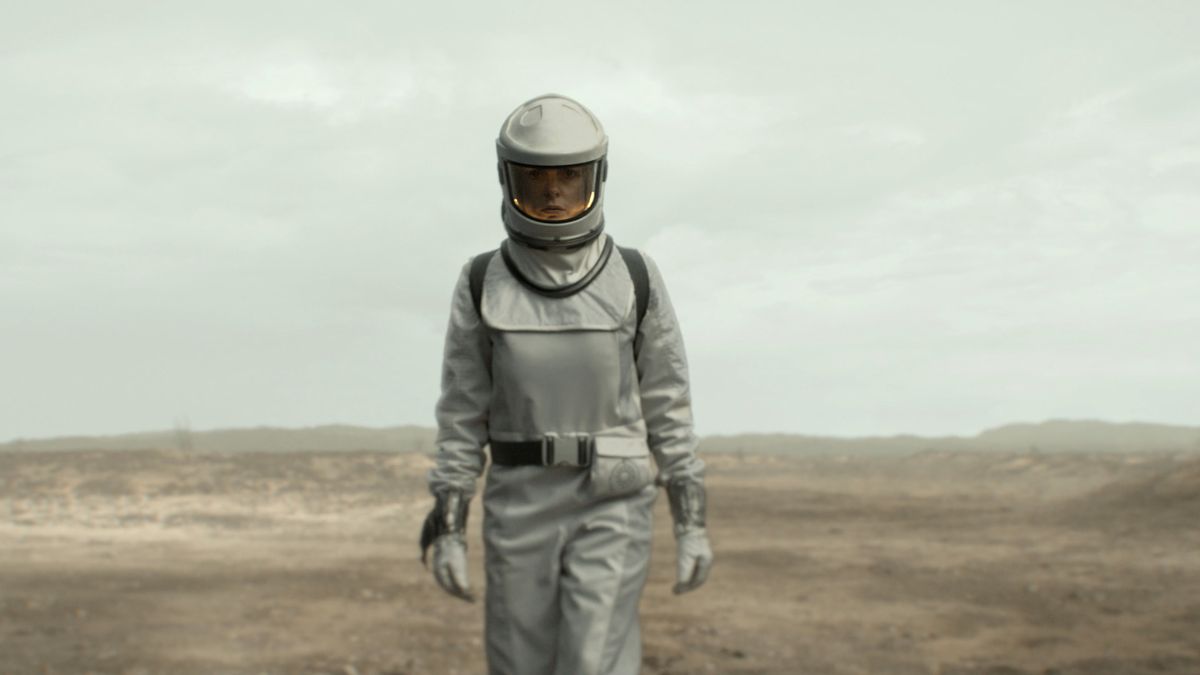 A woman wearing a protective silver suit walks in a wasteland