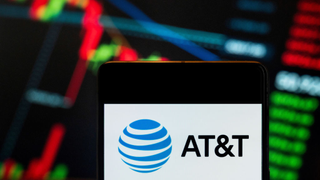 A mobile phone displays the AT&T logo in front of a blurred economic stock exchange index graph in the background