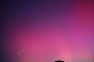 perseid meteor against a pink sky colored by auroras