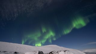 green curtains of light spread across the sky above snowcapped mountains.