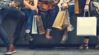 cropped close-up of five people sitting on a bench with shopping bags - only shows their legs