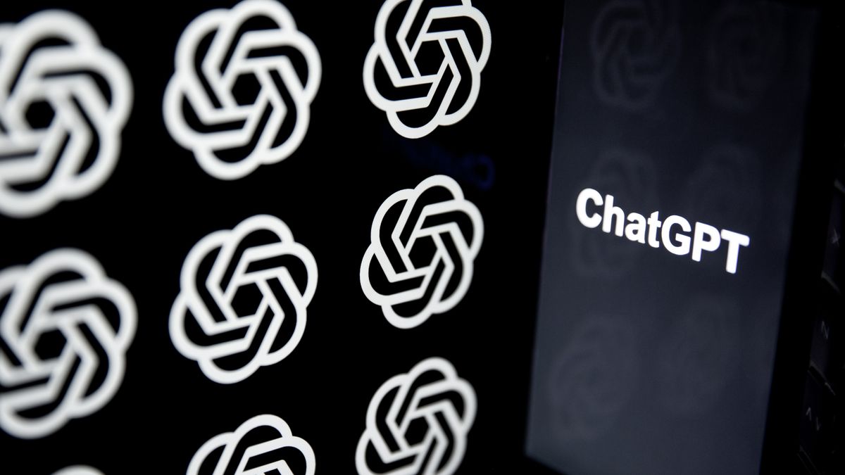 The word &quot;ChatGPT&quot; in white text on an otherwise black phone screen to the right of frame, with the OpenAI logo shown multiple times on a screen to the left of frame. The OpenAI logo is a circular knot, representing a combination of disciplines.