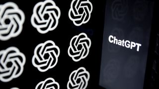 The word "ChatGPT" in white text on an otherwise black phone screen to the right of frame, with the OpenAI logo shown multiple times on a screen to the left of frame. The OpenAI logo is a circular knot, representing a combination of disciplines.