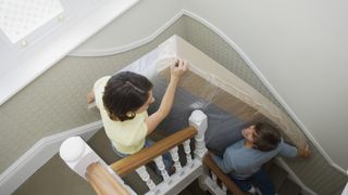 A couple carry a new mattress upstairs to their bedroom