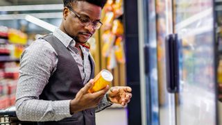 photo of a man checking the label on a yellow can that he&#039;s pullled from a fridge at a large grocery store