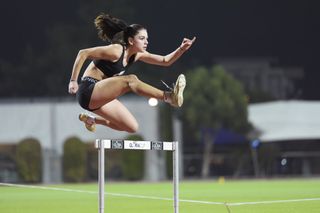 Olympic athlete jumping over a hurdle on a race track