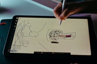 A close up of a child&#039;s hand as they use a stylus to draw on a tablet