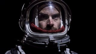 Close-up of a male astronaut in a space suit with a helmet looking up past the camera