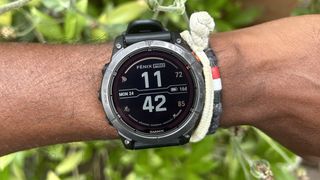 En Garmin Fenix 7 Pro runt en persons handled framför ett par gröna buskar i bakgrunden.