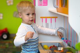 Little boy is playing in the preparation of a meal on a plastic toy kitchen.