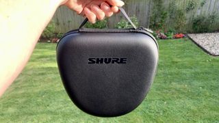 Shure Aonic 50 Gen 2 case, held in hand with a garden in the background