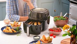 En svart Russell Hobbs Airfryer 4L står på en köksö med mat i behållaren och i skålar runtom.