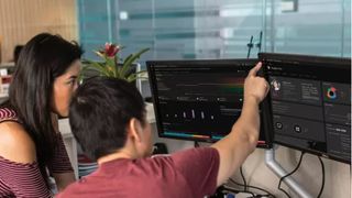 The back of two colleagues looking, and pointing at, a dual screen workstation in an office