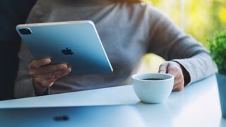 A woman holding and using Apple New Ipad Pro 2020 digital tablet with Apple MacBook Pro laptop computer while drinking coffee