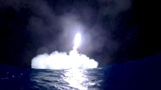 ocean-level view of a rocket coming down for a splashdown at night