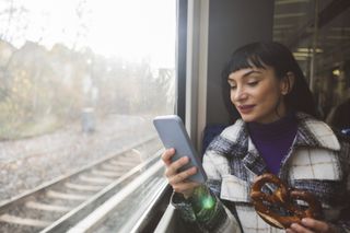 A woman holds a pretzel and uses a smart phone while on the train